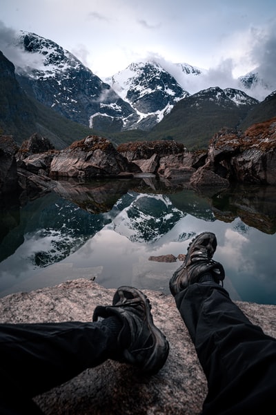 人在黑裤子和登山鞋坐在岩石白天湖附近
